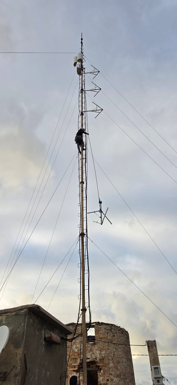Tower climber on the RadioActive 91.3 FM mast in Sifnos raising a new FM antenna into position